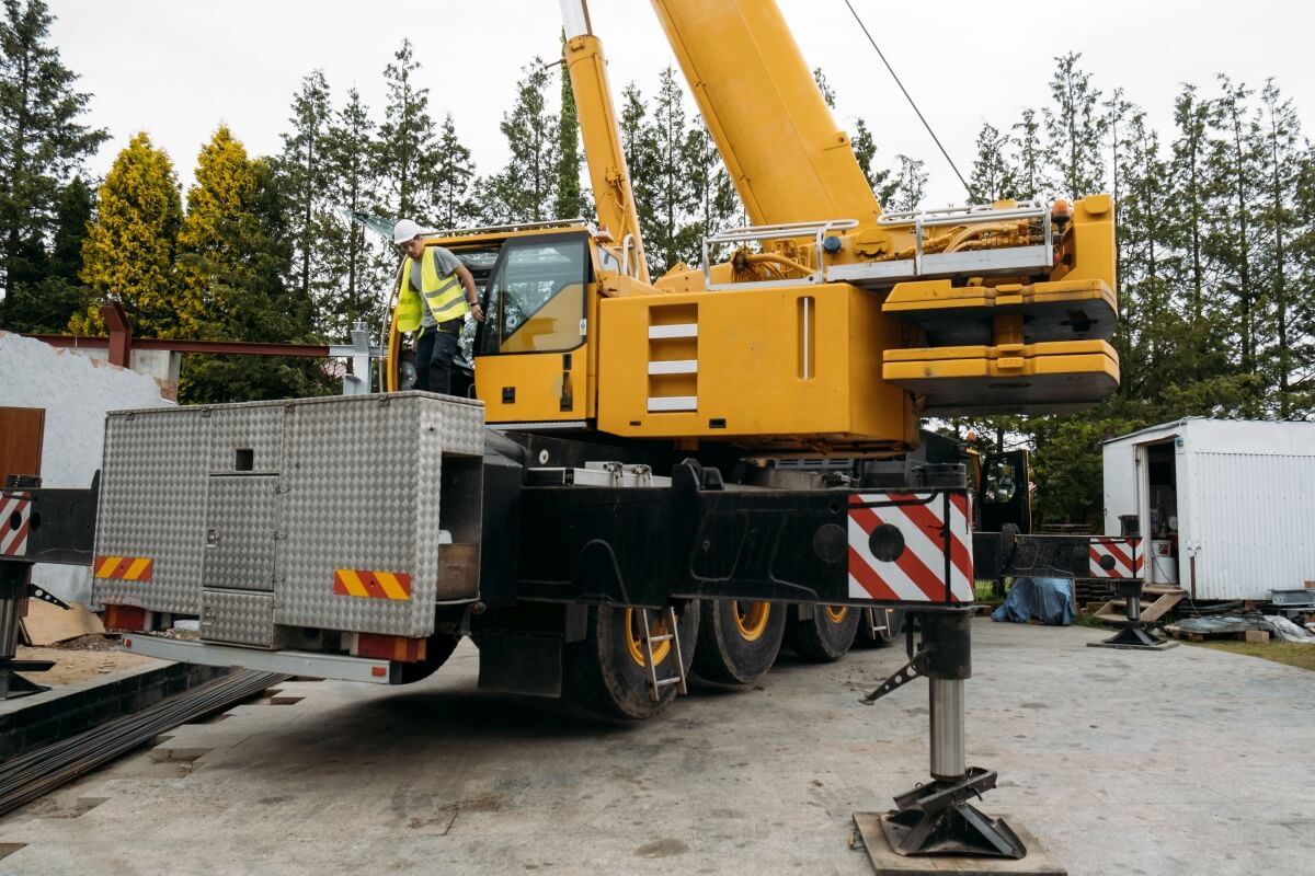 Żółty dźwig stoi na placu budowy, używając podkładów stabilizujących pod stopy HDS.