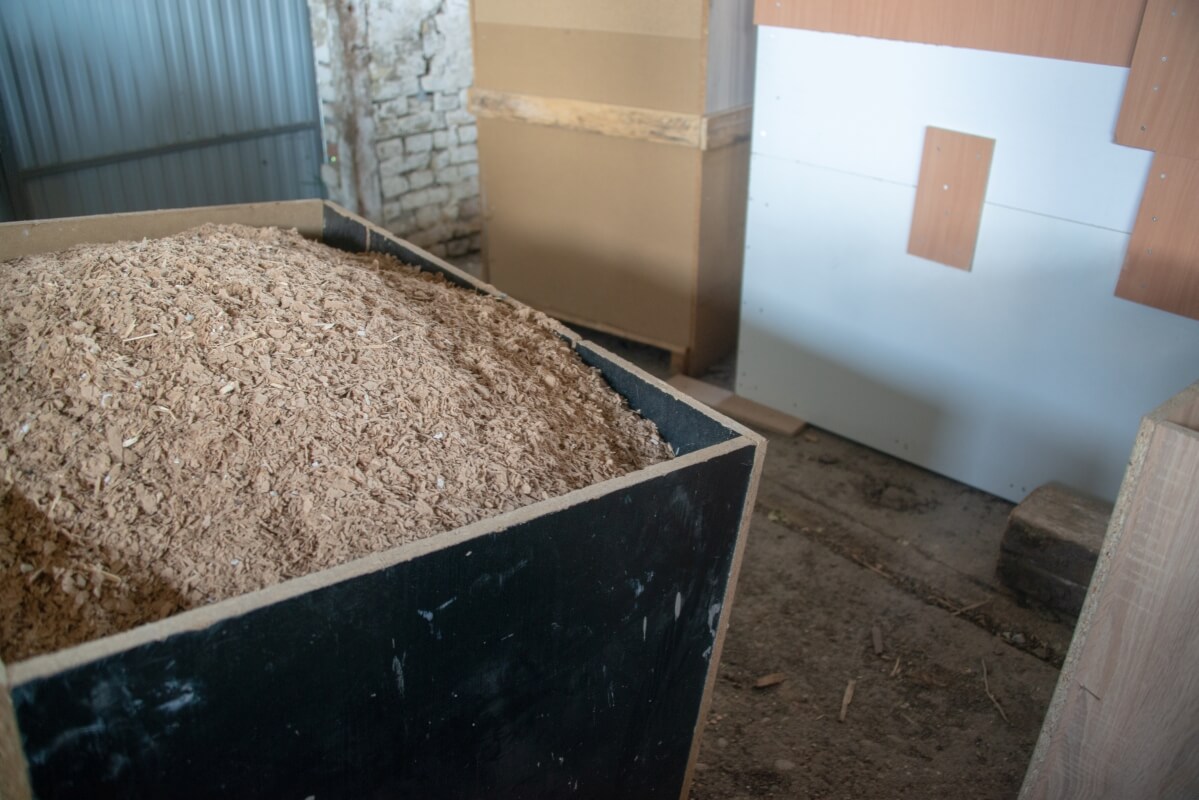 Stos wiórów drewnianych obok ściany z płytą z materiału takiego jak sklejka filmowana obustronnie.