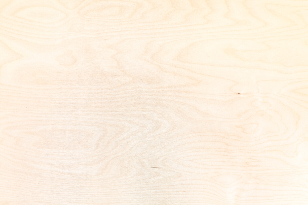 Zbliżenie na fakturę, jaką ma sklejka drewniana z widocznymi sękami i słojami.