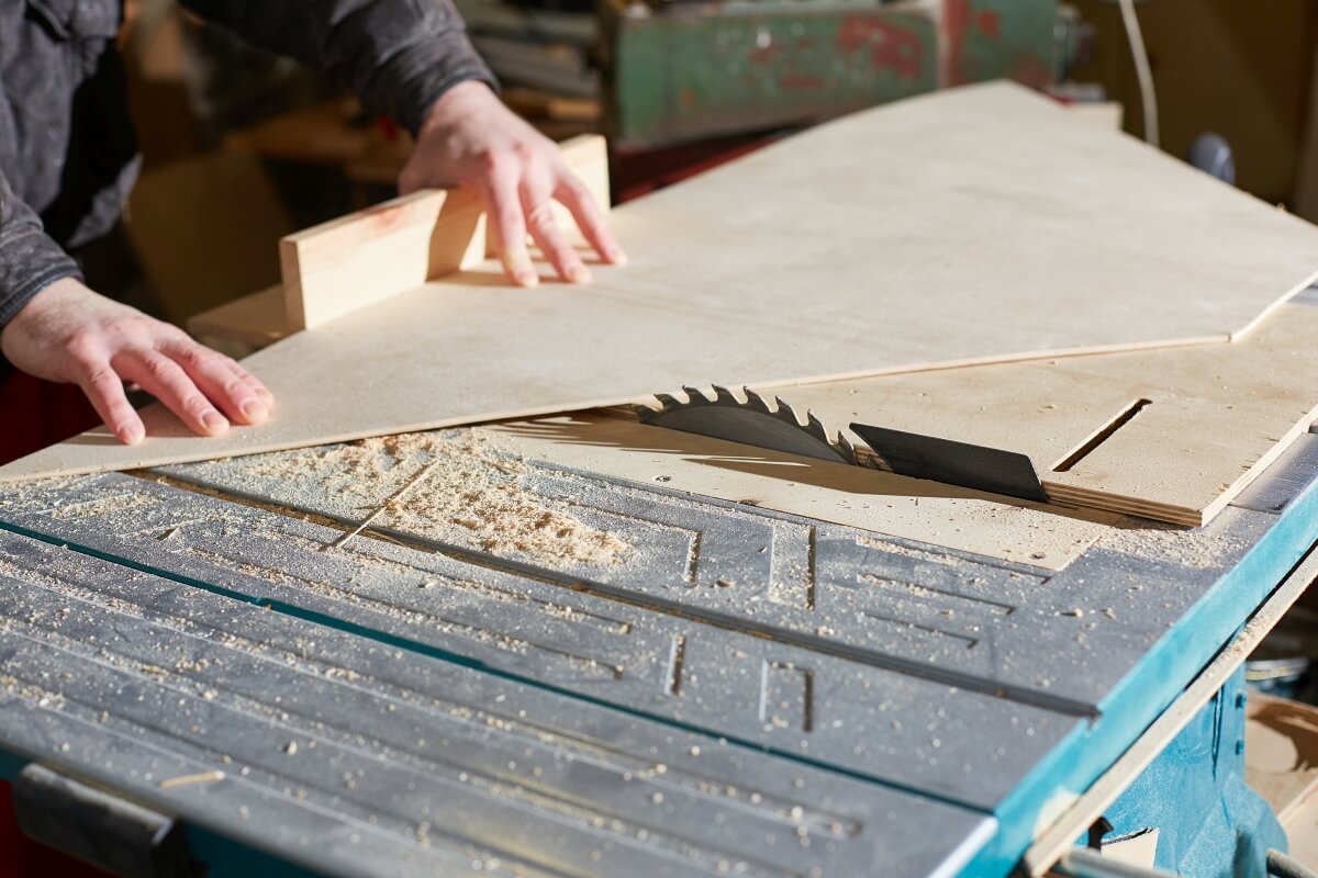 Rzemieślnik przycina sklejkę na wymiar przy użyciu piły stołowej.