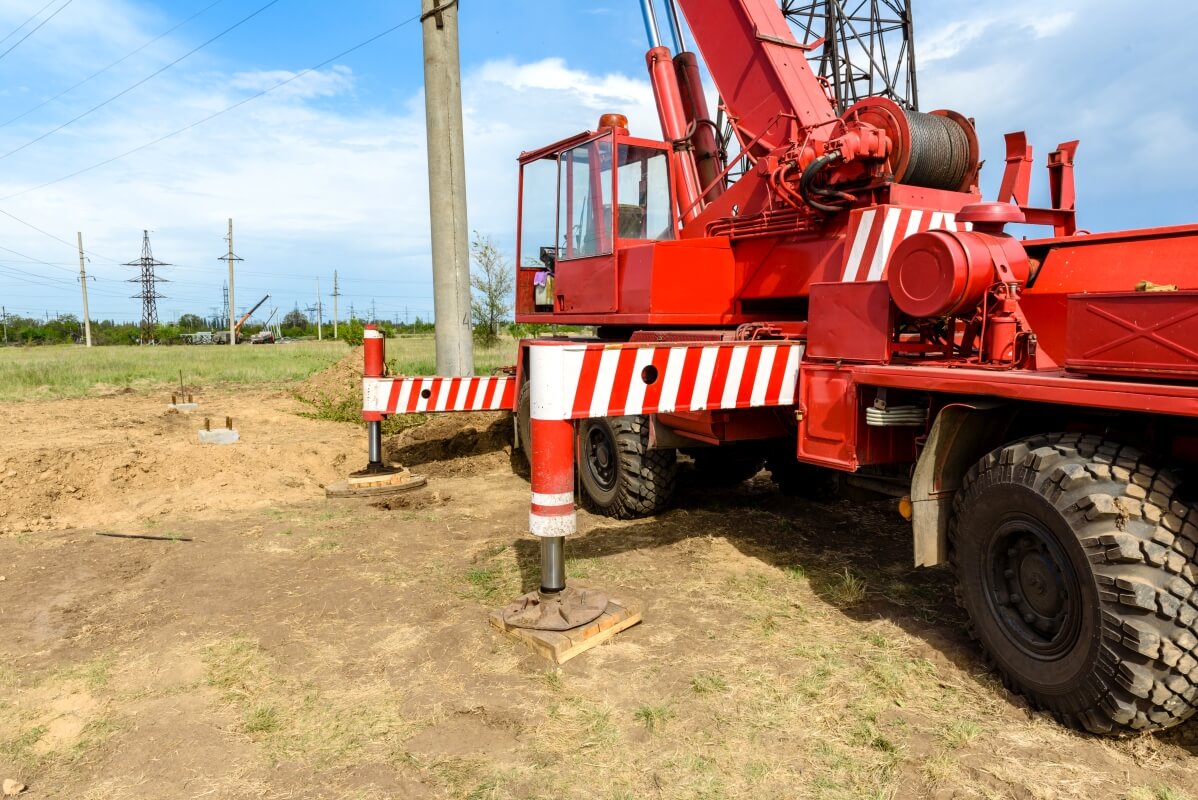 Czerwony dźwig z podłożonymi podkładami stabilizującymi pod stopy HDS na placu budowy.