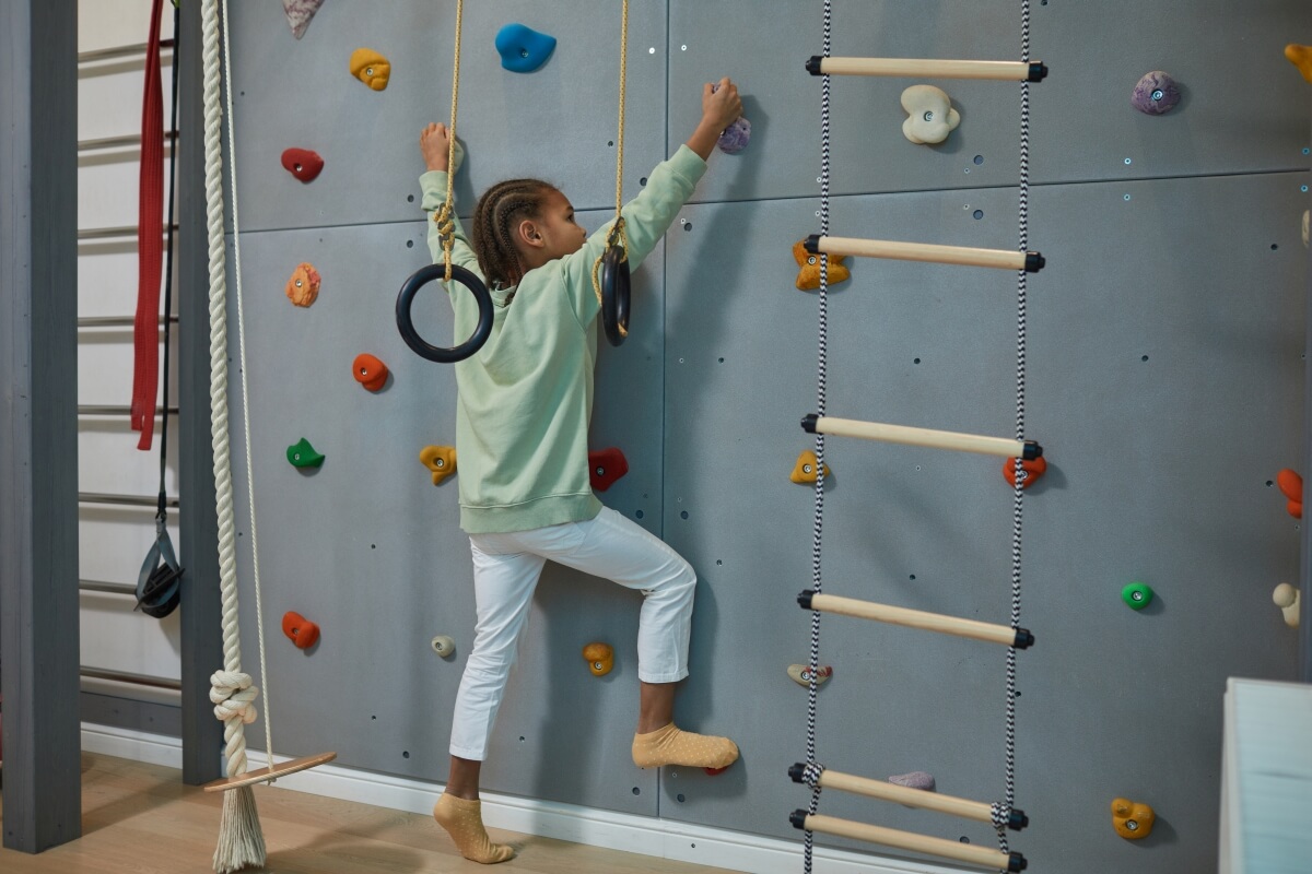 Dziewczynka wspina się na ściance wspinaczkowej domowej ze sklejki.