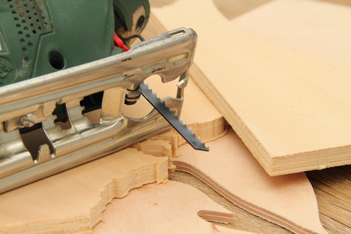 Piła do drewna leży obok pociętych arkuszy: sklejka na wymiar.